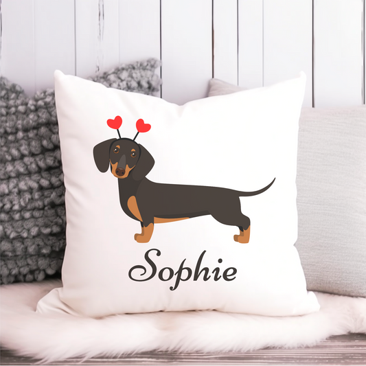 A white square cushion cover featuring a black and tan dachshund with red heart-shaped antennae. The name "Sophie" is printed below the dog.