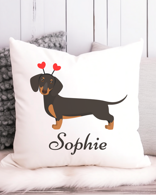 A white square cushion cover featuring a black and tan dachshund with red heart-shaped antennae. The name "Sophie" is printed below the dog.