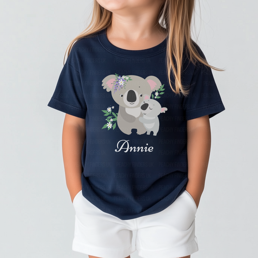 Little girl wearing a navy personalised T-shirt featuring a cute mother and baby koala with floral accents, custom name printed below.
