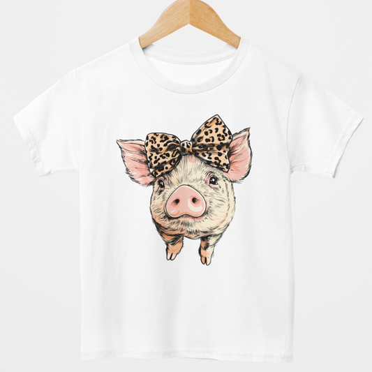 Kids white t-shirt on a wooden hanger featuring a cute piglet graphic with a leopard print bow on its head.