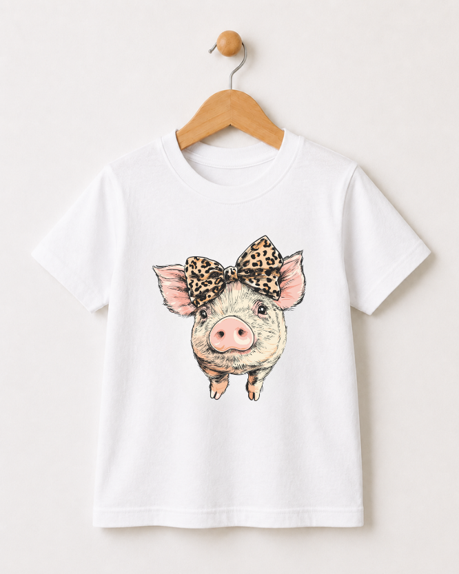 Girls white t-shirt with a pig wearing a leopard print bow styled on a wooden hanger against a white background