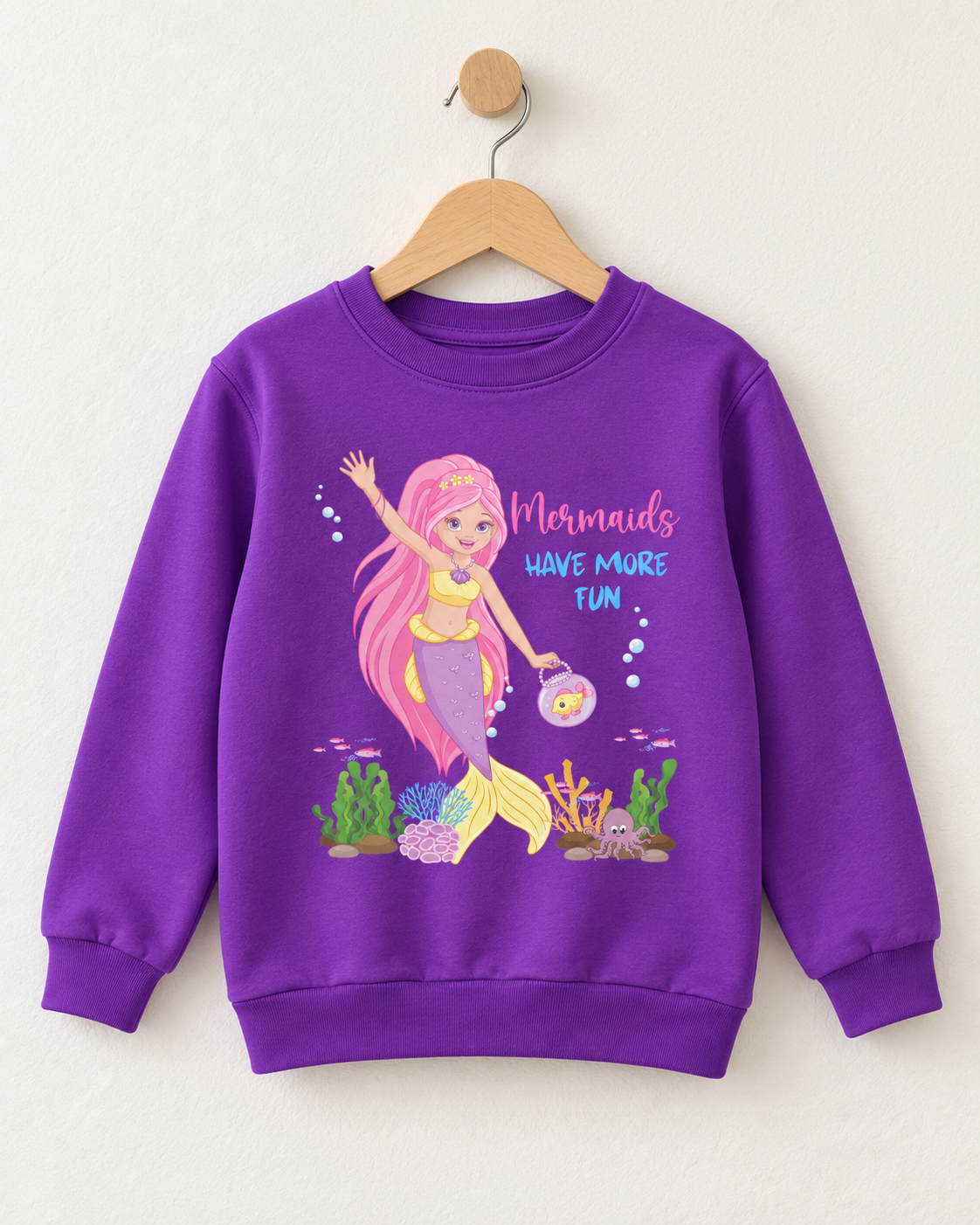 Girls’ purple “Mermaids Have More Fun” sweatshirt displayed on a wooden hanger, featuring a pink-haired mermaid and underwater scene.
