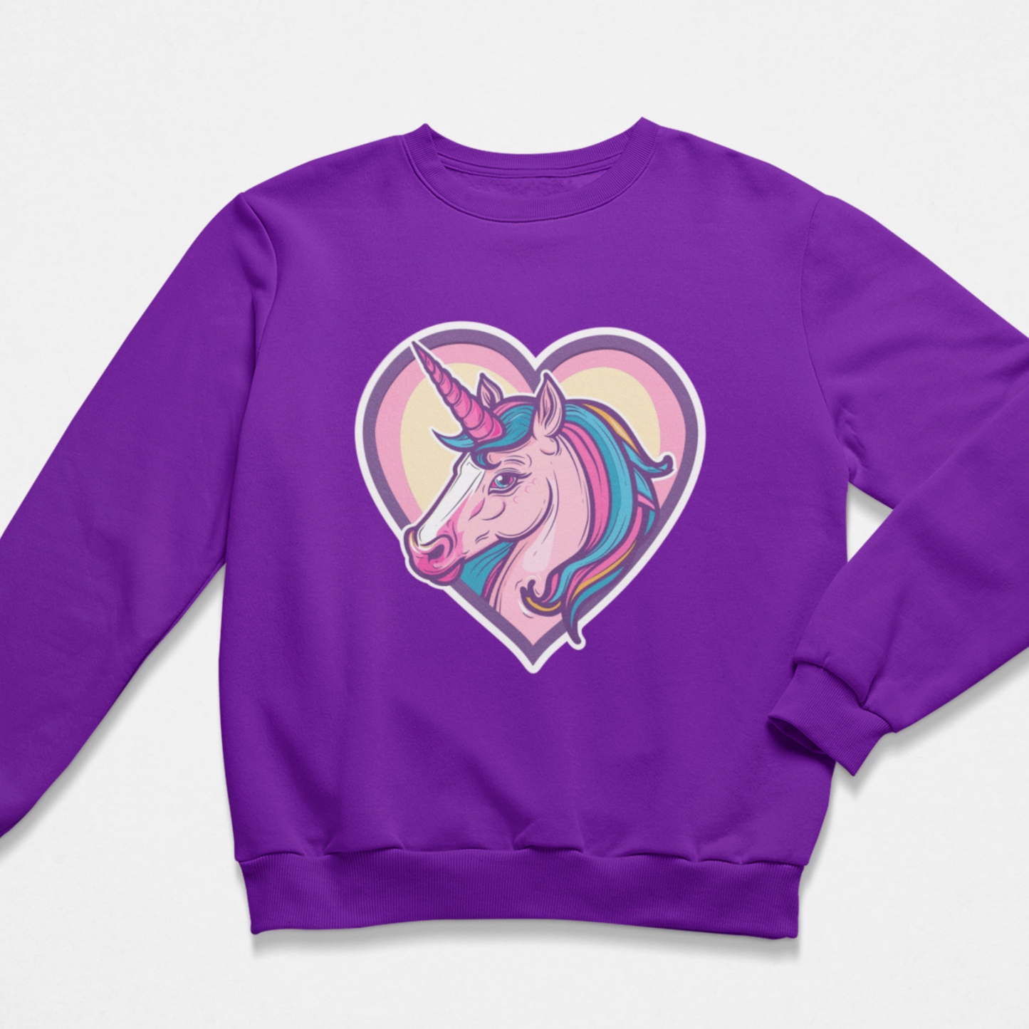 A girls purple crewneck sweatshirt featuring a colourful graphic of a unicorn inside a heart on the chest, displayed against a light grey background.
