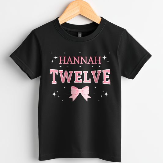 Custom girls 12th birthday t-shirt with name, pink bow and stars on black cotton tee on wooden hanger