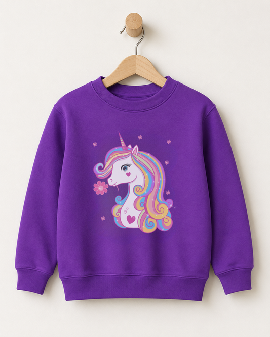 A girls purple crewneck sweatshirt featuring a colourful cartoon unicorn graphic on the front, hanging on a wooden hanger against a plain off-white wall.