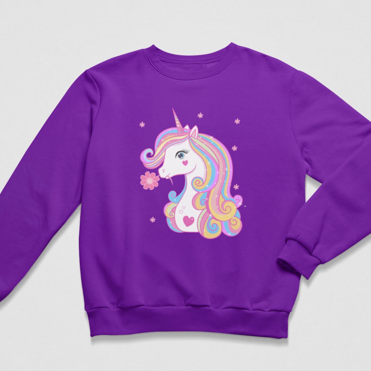 A girls purple crewneck sweatshirt featuring a colourful cartoon unicorn graphic on the front, set against a light grey background.
