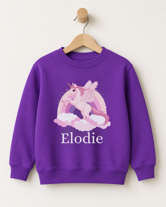 Purple personalised girls’ sweatshirt featuring a white winged unicorn, pastel rainbow, clouds and the name Elodie, displayed on a wooden hanger.