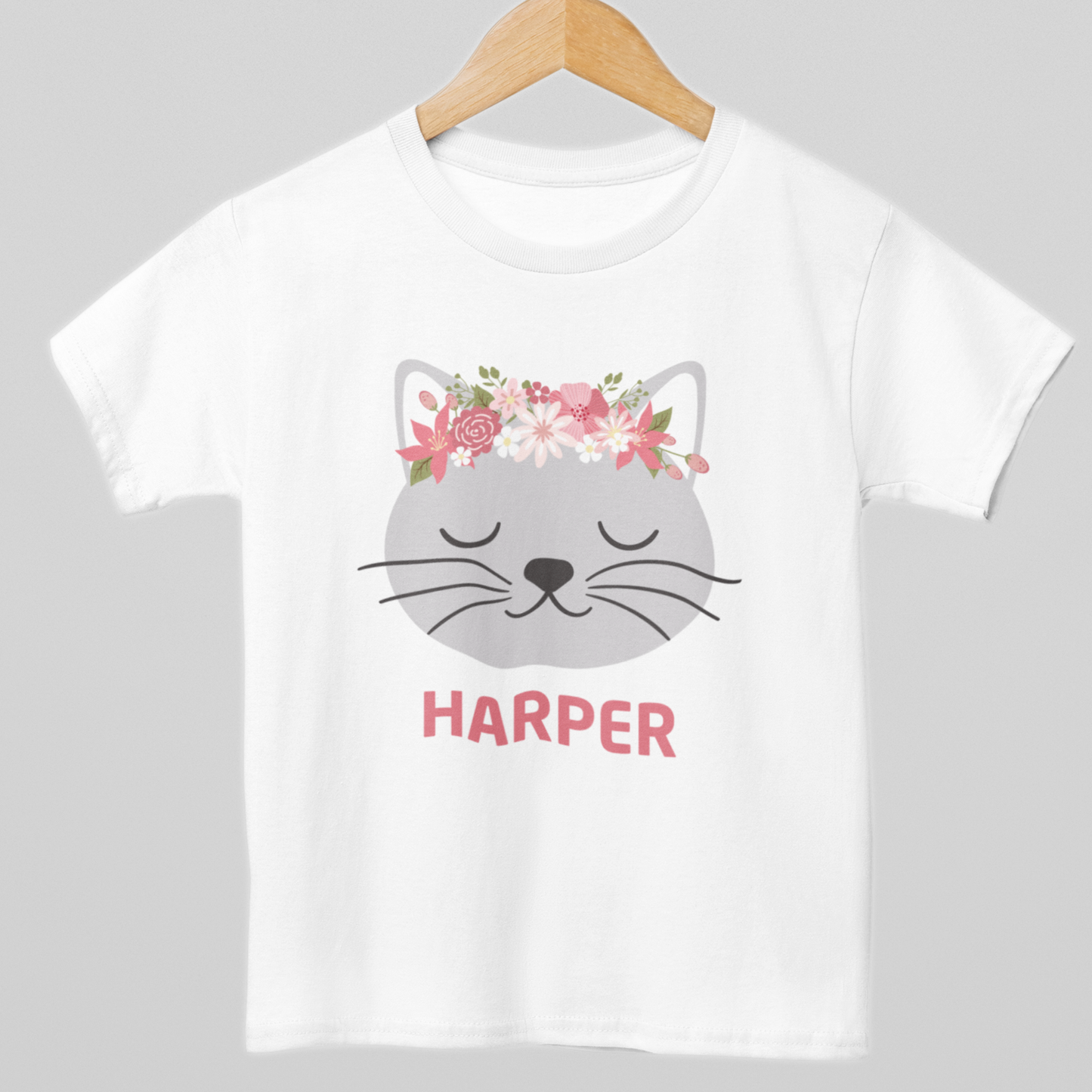 Girls white cotton t-shirt, styled on a wooden hanger - personalised floral cat design with custom name printed under a grey kitten face with pink flower crown
