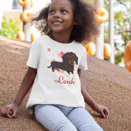 Child wearing a white t-shirt with a dachshund graphic and the name 'Leah' on a playground.