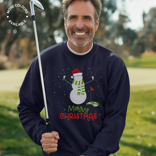 Man wearing a navy Christmas sweatshirt featuring a golf ball snowman holding golf clubs with a Santa hat and green scarf, standing on a putting green
