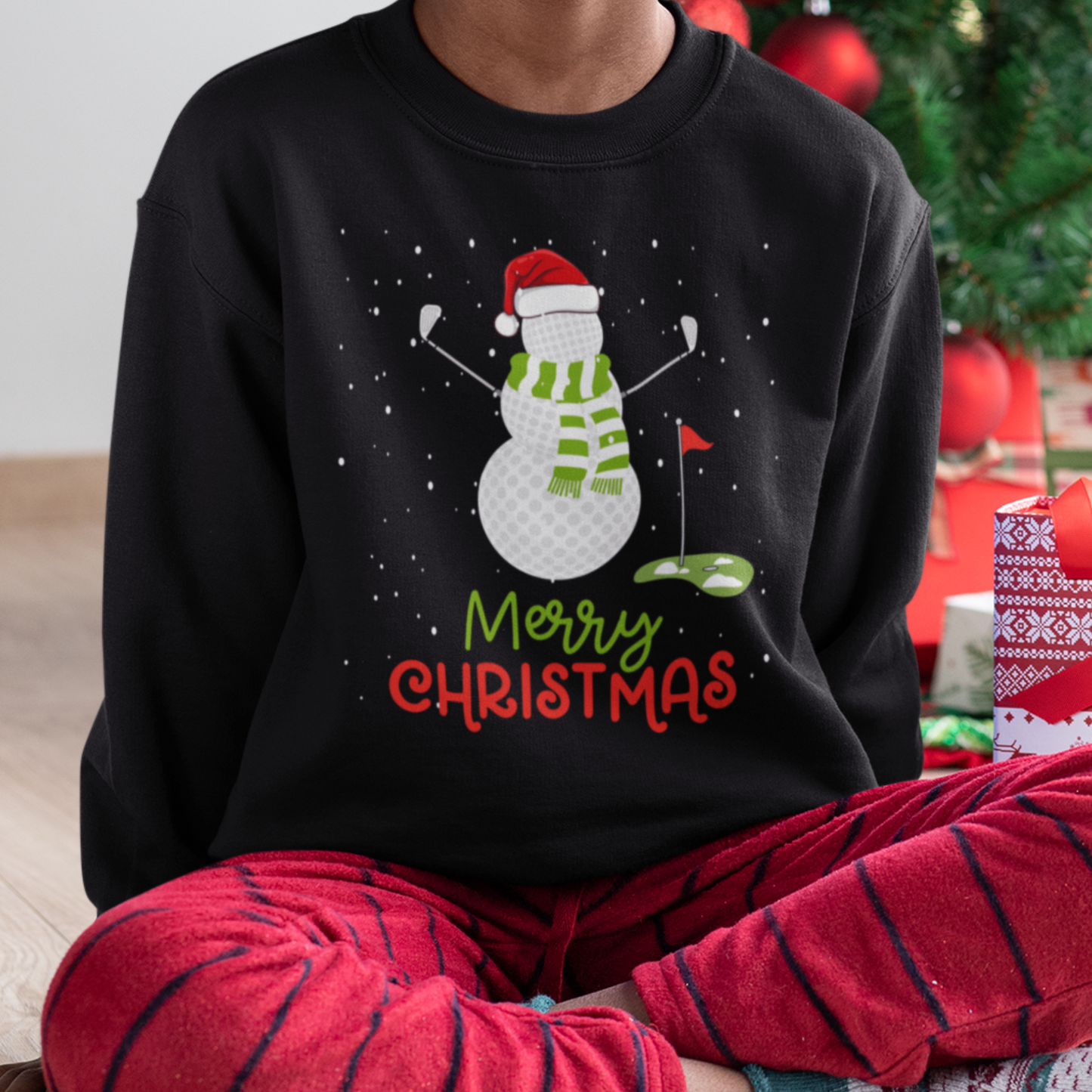 Child wearing a black Christmas sweatshirt with a snowman made of golf balls holding golf clubs, green scarf and Santa hat, with Merry Christmas text