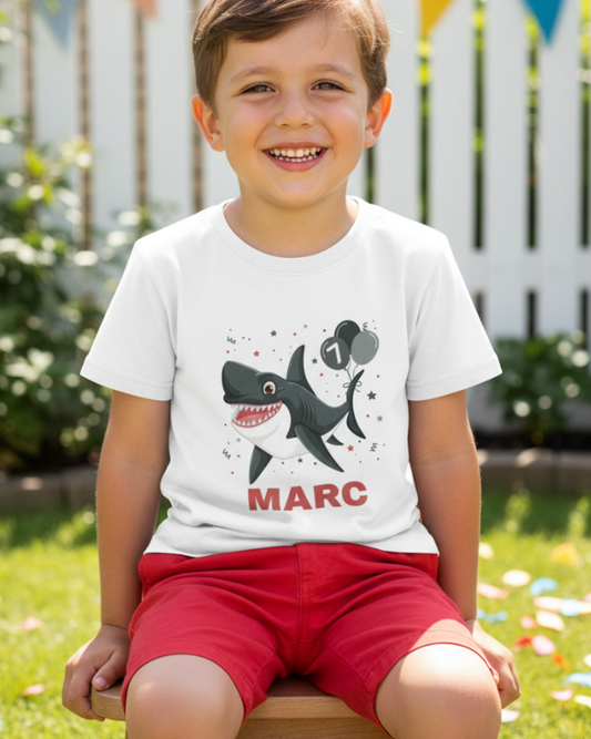 Smiling young boy wearing personalised shark birthday t-shirt with name Marc, outdoor garden setting
