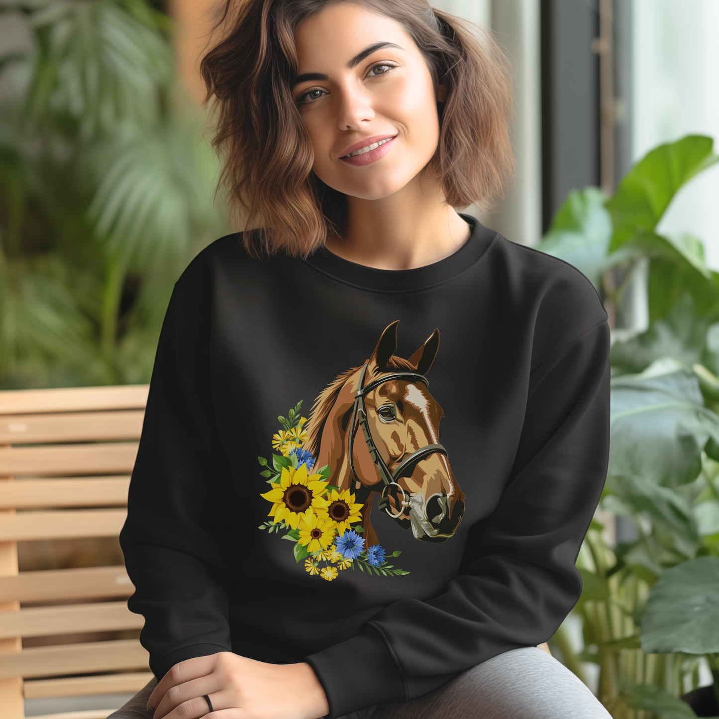 Women sitting on a chair wearing a black sweatshirt with a printed design of a brown horse with a sunflower arrangement