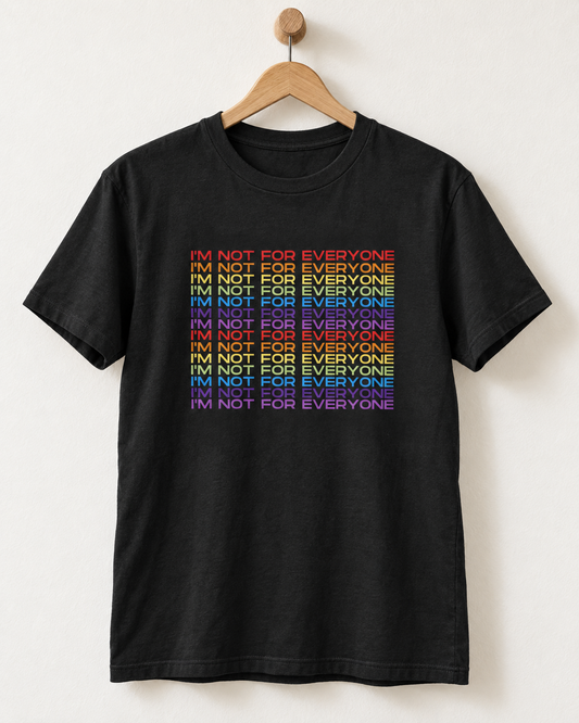 A black short-sleeve t-shirt hanging on a wooden hanger against a light off-white wall. The shirt features a graphic print of the phrase 'I'M NOT FOR EVERYONE' repeated in a vertical stack, with each line shifted to the right in a rainbow gradient of red, orange, yellow, green, blue, and purple.