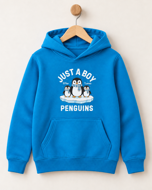 A bright blue kids' pullover hoodie hanging on a wooden hanger against a light beige wall. The hoodie features a front graphic with the text 'JUST A BOY' and 'PENGUINS' in white, surrounding an illustration of three penguins on a piece of ice.