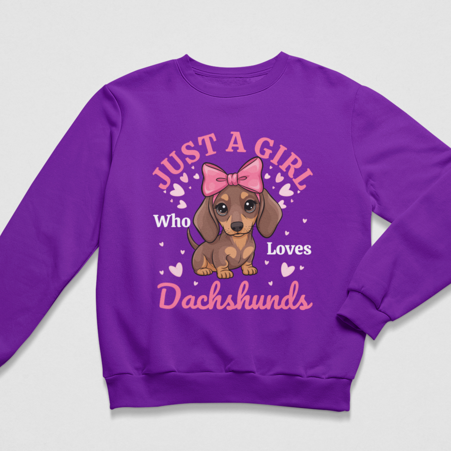 A kids purple crewneck sweatshirt featuring a graphic print of a brown dachshund with a pink bow, surrounded by the text 'JUST A GIRL Who Loves Dachshunds' in pink and white, on a light gray background.