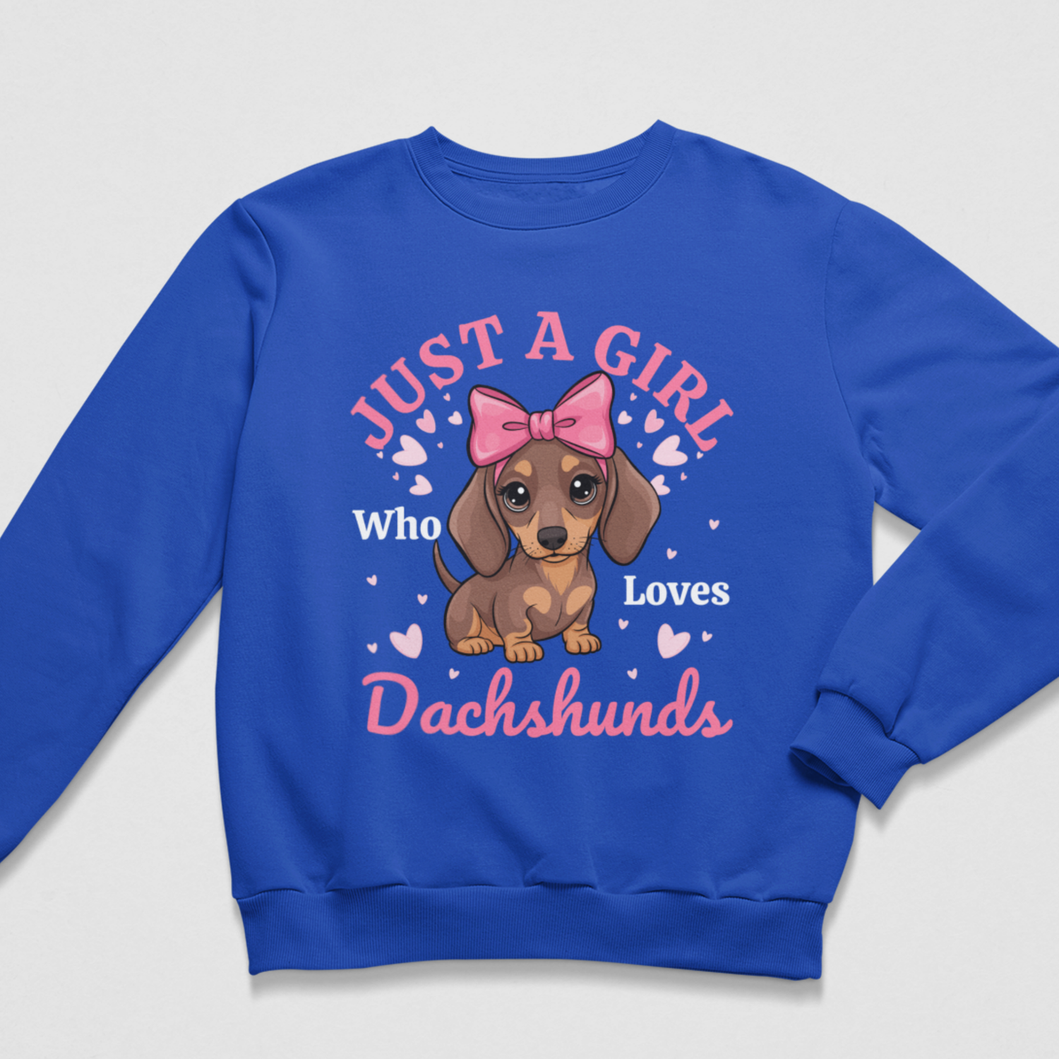 A kids royal blue crewneck sweatshirt featuring a cartoon dachshund wearing a pink bow, surrounded by the text 'JUST A GIRL Who Loves Dachshunds' in pink and white, with small pink hearts.