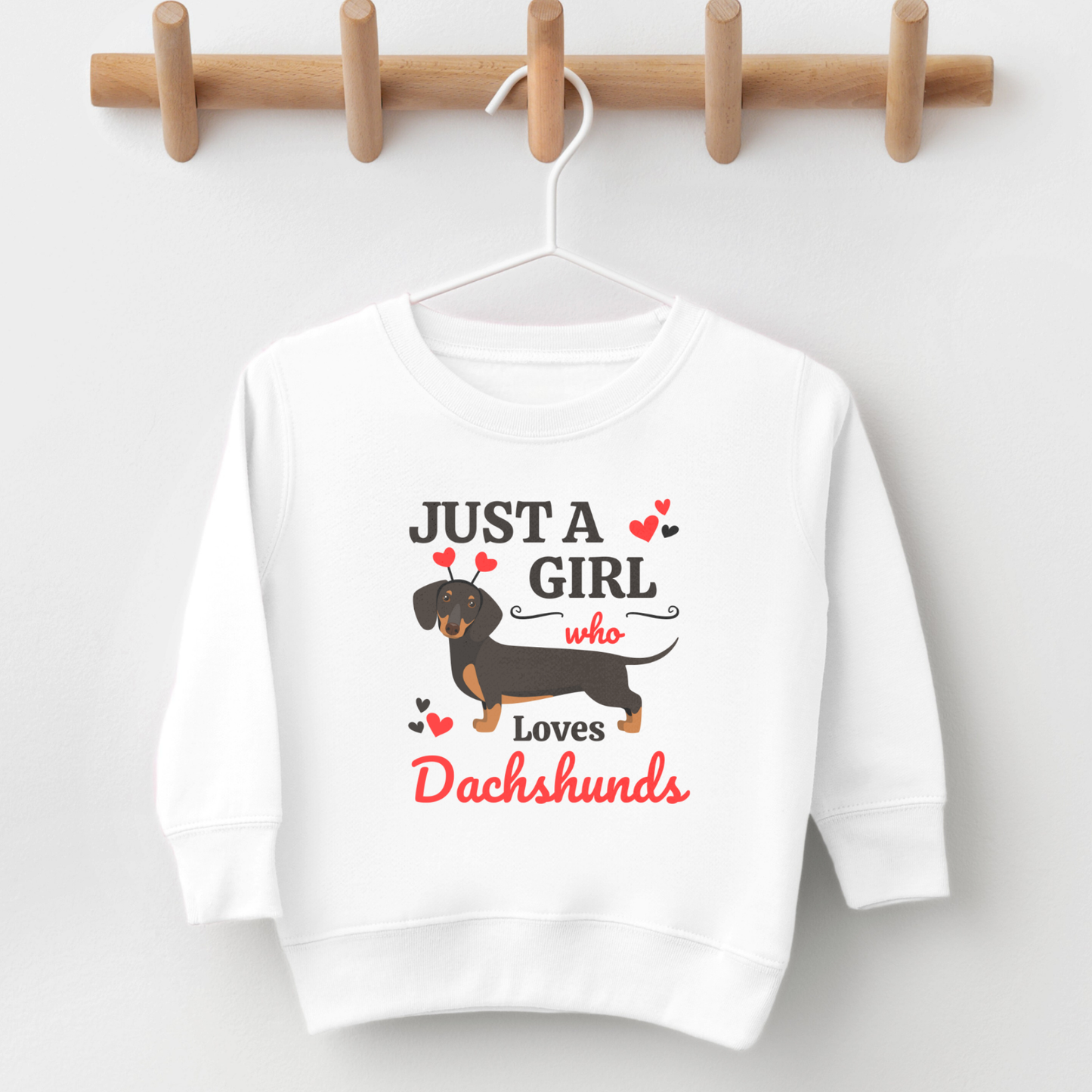 White children’s “Just A Girl Who Loves Dachshunds” sweatshirt displayed on a hanger against a neutral wall.