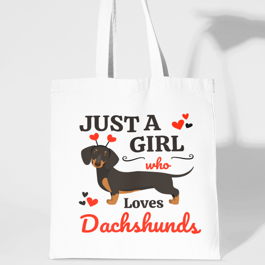 A person holding a white cotton tote bag with the text 'JUST A GIRL WHO LOVES DACHSHunds' and an illustration of a dachshund on it.