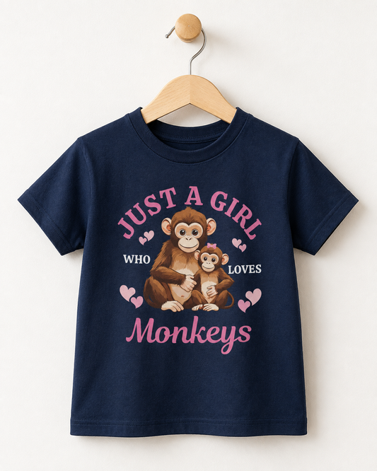 A navy blue short-sleeve kids t-shirt hanging on a wooden hanger against a plain off-white wall. The shirt features a graphic print of a mother monkey and her baby, surrounded by pink hearts and the text 'JUST A GIRL WHO LOVES Monkeys' in pink and white.