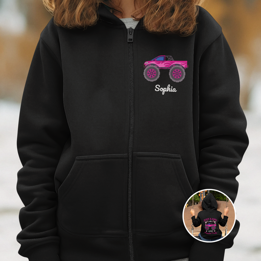 The girl wears a child's-sized black zip-hoodie with a printed motif of a pink monster truck and the name Sophia underneath. A small circular picture at the bottom shows the back of the zip hoodie with a printed design with the wording, Just a Girl who Loves Monster Trucks.