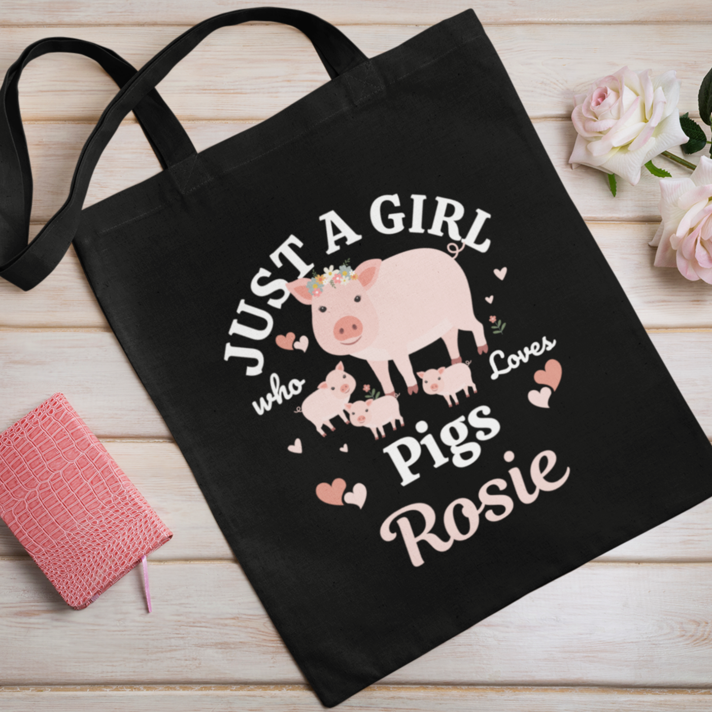 Kids black tote bag with a pig design and text on a wooden surface with flowers.