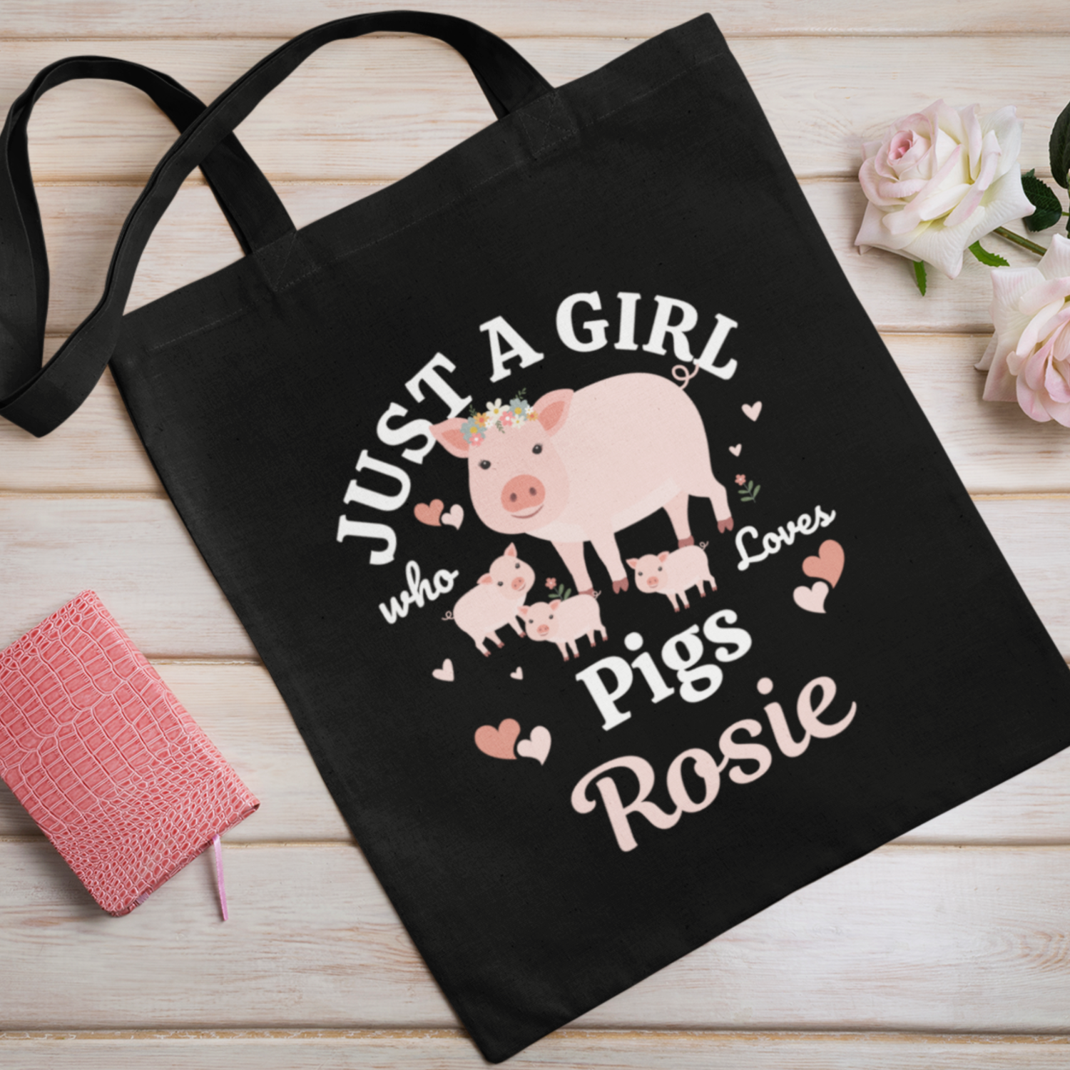 Kids black tote bag with a pig design and text on a wooden surface with flowers.
