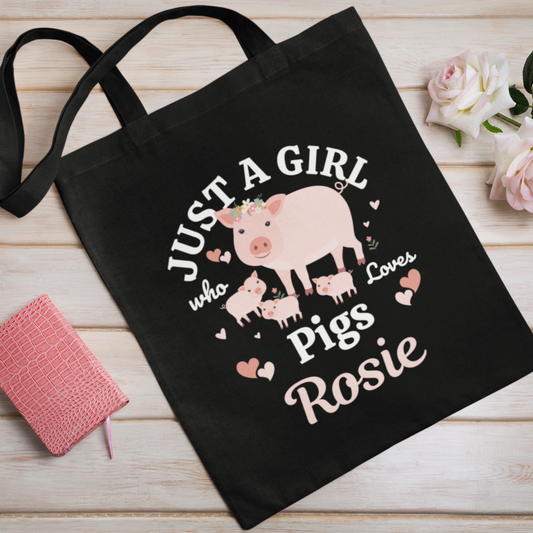 Kids black tote bag with a pig design and text on a wooden surface with flowers.