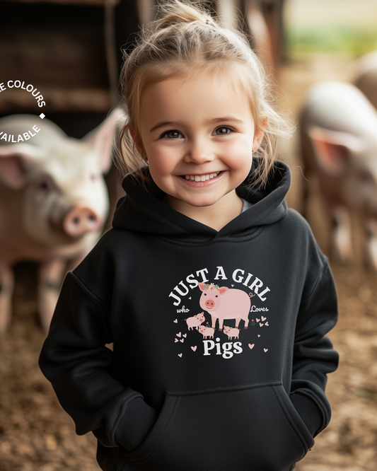Young girl wearing a black hoodie with a pig design and text, standing in front of pigs on a farm.