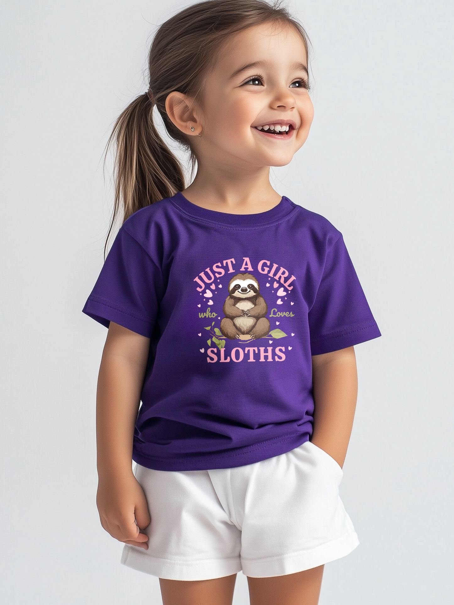 Little girl wearing a purple t-shirt with a cute sloth design and the text "Just a Girl Who Loves Sloths", smiling and posing with hands in pockets.