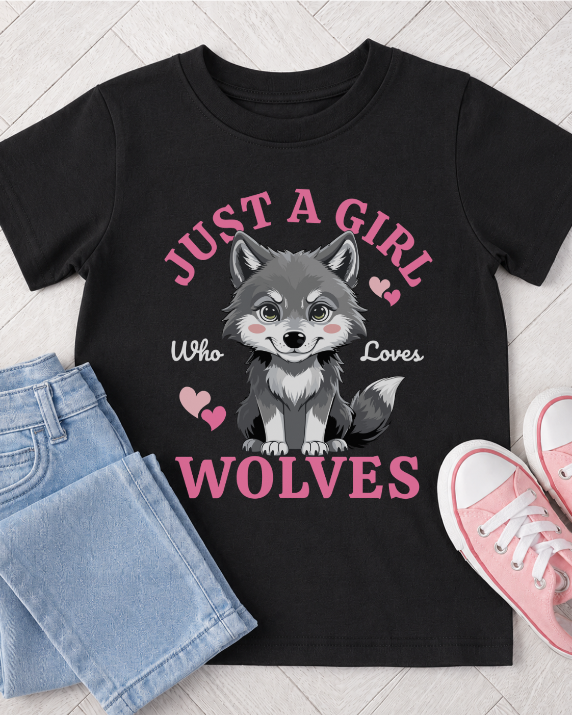 Black girls T-shirt featuring a cute grey wolf with pink hearts and bold “Just a Girl Who Loves Wolves” text, styled in a flat lay with light blue jeans and pink trainers.
