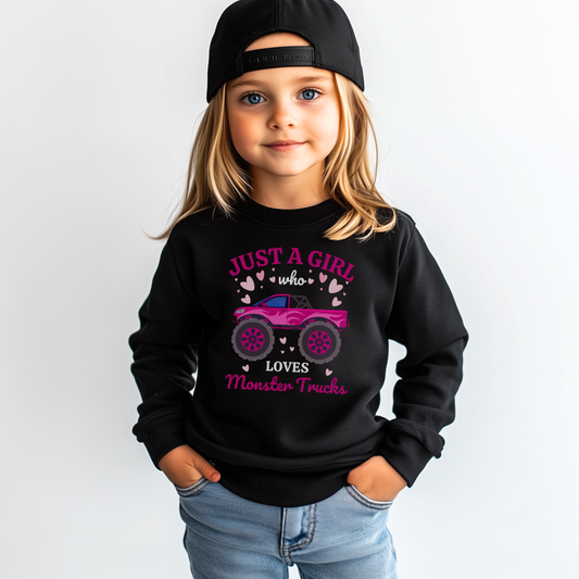Young girl wearing a black “Just a Girl Who Loves Monster Trucks” sweatshirt with pink monster truck print, hands in pockets