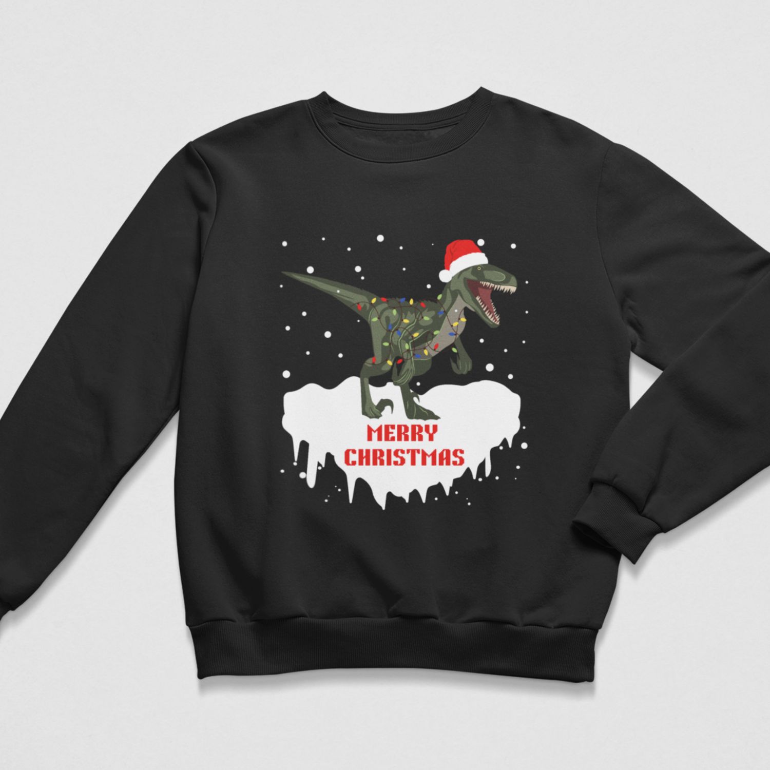 A kids black crewneck sweatshirt featuring a graphic of a green dinosaur wearing a red Santa hat and holiday lights, standing on a white snowy shape with the text 'MERRY CHRISTMAS' in red, shown on a light grey background.