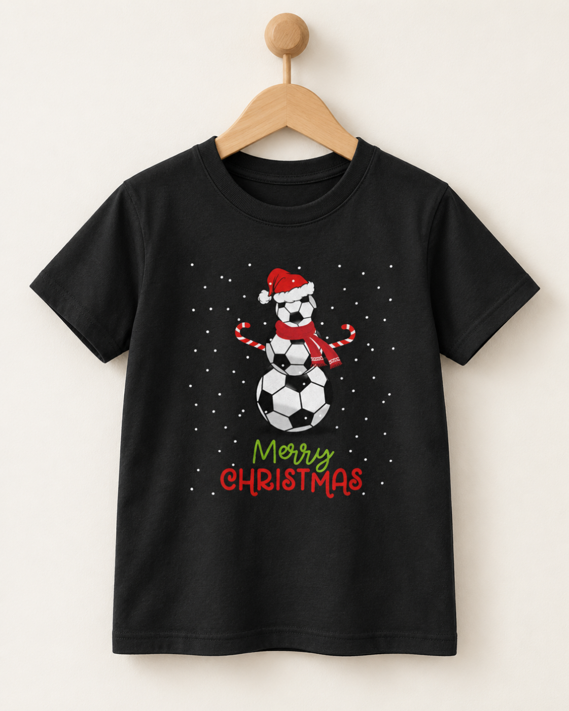 Kids black Christmas T-shirt on a wooden hanger featuring a snowman made from stacked footballs, a Santa hat, scarf and Merry Christmas lettering.