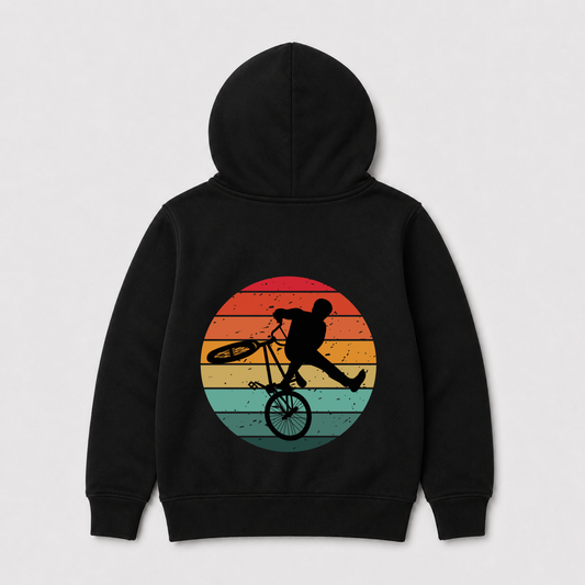 A black pullover hoodie shown from the back, featuring a large graphic print of a BMX rider in black silhouette riding in front of a retro circular sunset with orange, yellow, and teal stripes.