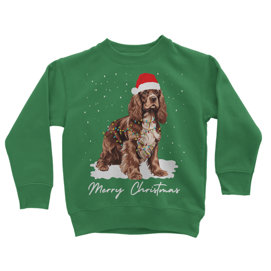 Kids green Christmas sweatshirt featuring a brown and white Cocker Spaniel, wearing Santa hat, wrapped in Xmas lights with falling snow design.