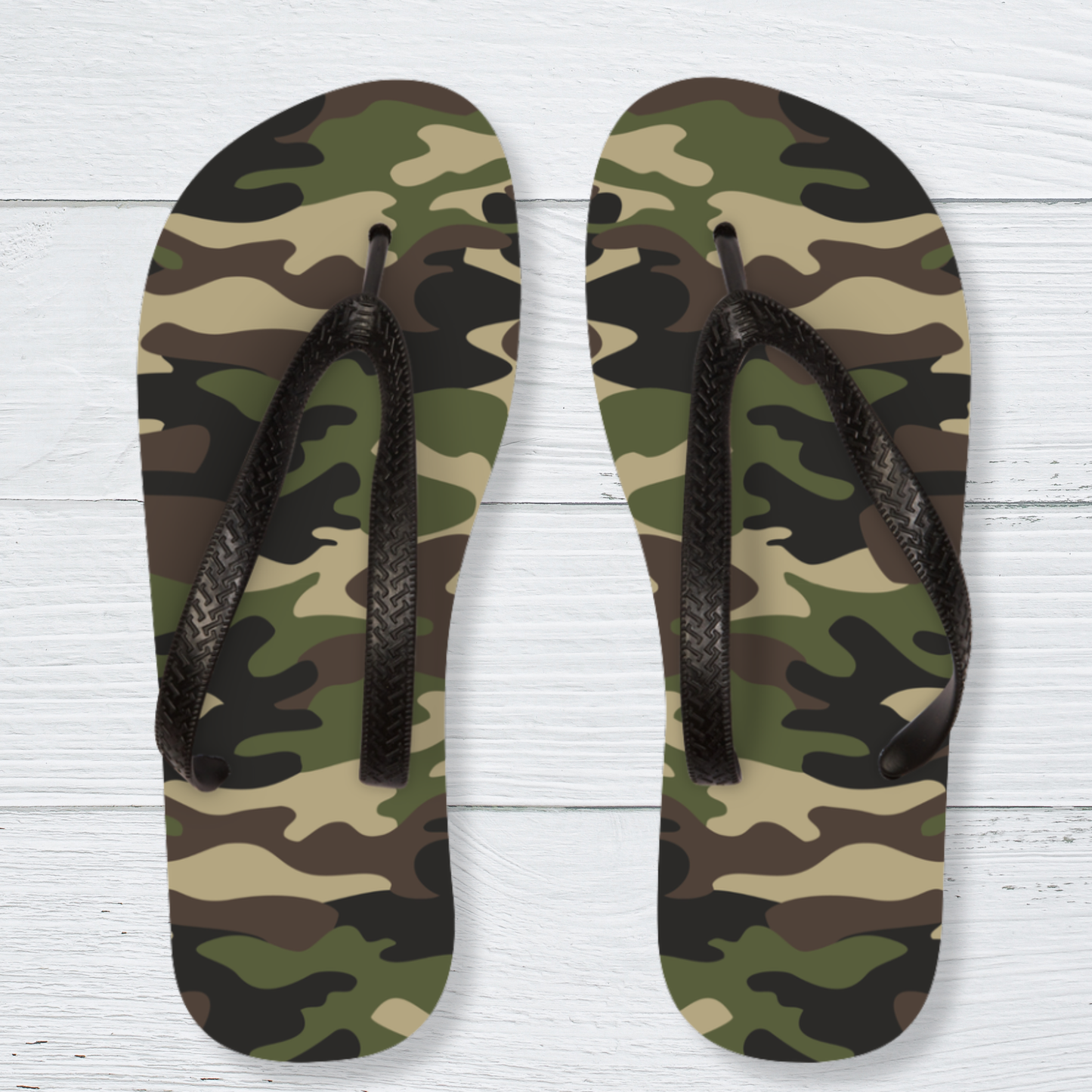 Kids camouflage flip-flops with textured black straps, shown on a white wooden background with an olive green, khaki, brown and black camo pattern.