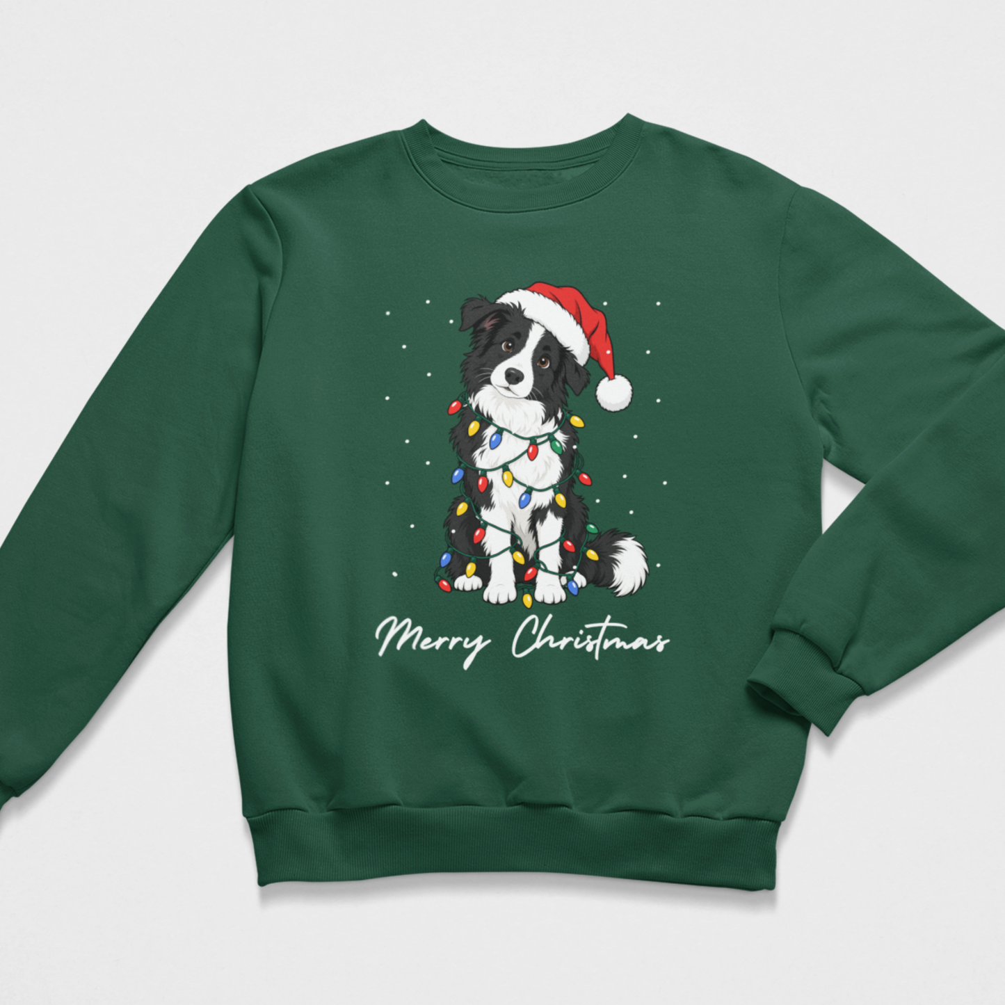 dark green crewneck Christmas sweatshirt shown in a clean flat lay. It displays an illustration of a festive Border Collie wearing a Santa hat, wrapped in glowing fairy lights, and positioned above white script reading "Merry Christmas"