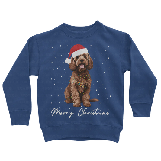 Kids royal blue sweatshirt with a Christmas-themed design of a brown cockapoo wearing a Santa hat, wrapped in fairy lights with falling snow and the text 'Merry Christmas'.