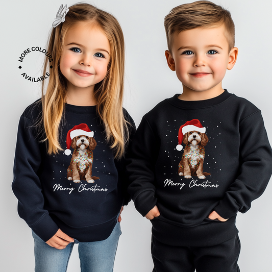 Two children, a girl and a boy, wearing dark-colored sweatshirts with a graphic of a Cavapoo dog wearing a Santa hat and fairy lights, and the text 'Merry Christmas'.