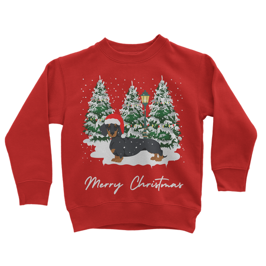 Kids red Christmas sweatshirt featuring a festive dachshund in a Santa hat, standing in front of snowy Christmas trees with a lamp post.