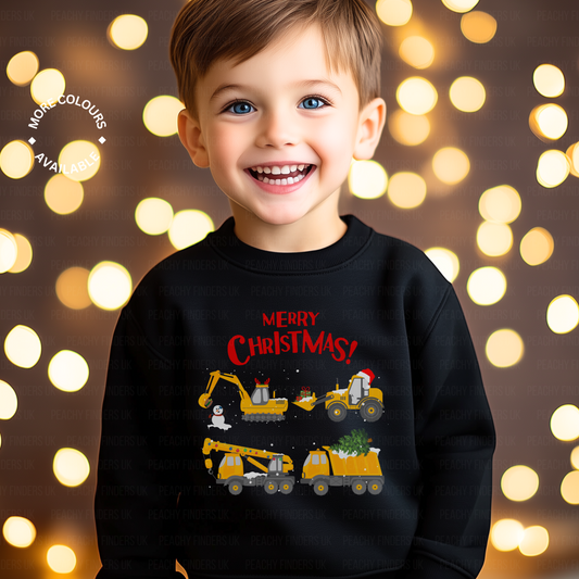 A child wearing a black sweatshirt with a 'Merry Christmas' construction vehicles and festive digger on it, standing against a backdrop with Christmas lights.