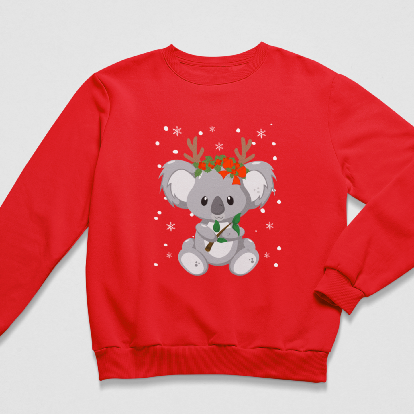 Bright red kids festive sweatshirt printed with a grey Christmas koala, reindeer antlers, holly-style flowers, green foliage and scattered snowflake details.