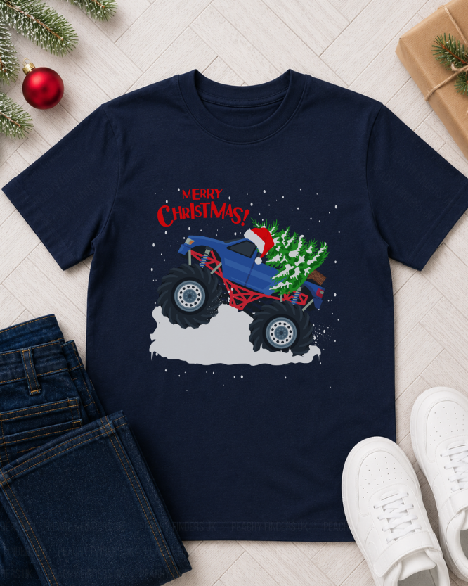 Kids navy blue t-shirt with Christmas-themed graphic of a monster truck carrying a tree, surrounded by festive decor on a light wooden floor.