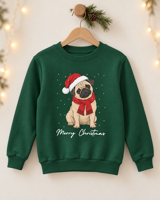 A children's dark green crewneck sweatshirt hanging on a wooden hanger decorated with a pine branch and fairy lights. The sweatshirt features a graphic of a pug wearing a red Santa hat and matching red scarf, with 'Merry Christmas' written in white script below.