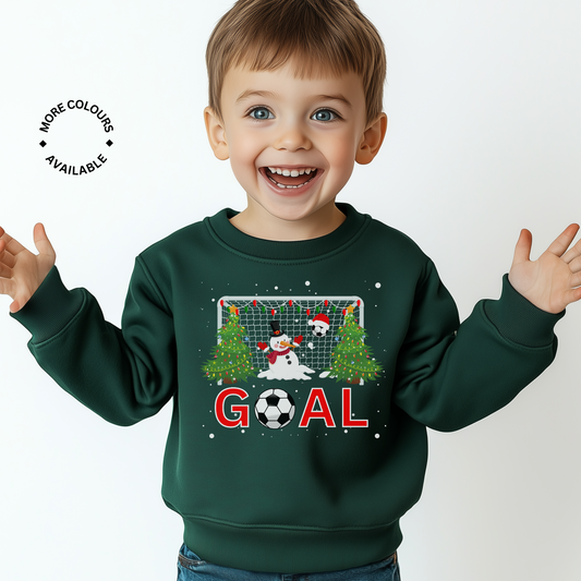Young boy wearing a dark green Christmas sweatshirt featuring a festive football goal design with a snowman goalie, decorated Christmas trees, and the word "GOAL".