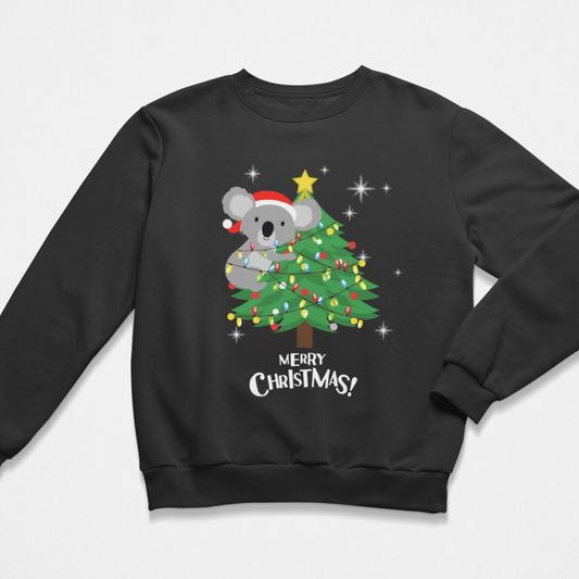 A kids black crewneck sweatshirt featuring a festive graphic of a grey koala wearing a red Santa hat next to a green Christmas tree with colourful lights and a gold star. Below the illustration, the text 'MERRY CHRISTMAS!' is printed in white.