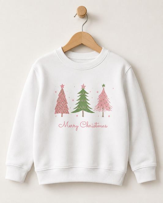 A children's white crewneck sweatshirt hanging on a wooden hanger against a light beige wall. The sweatshirt features a graphic of three Christmas trees in pink and green with the words 'Merry Christmas' written below in pink script.