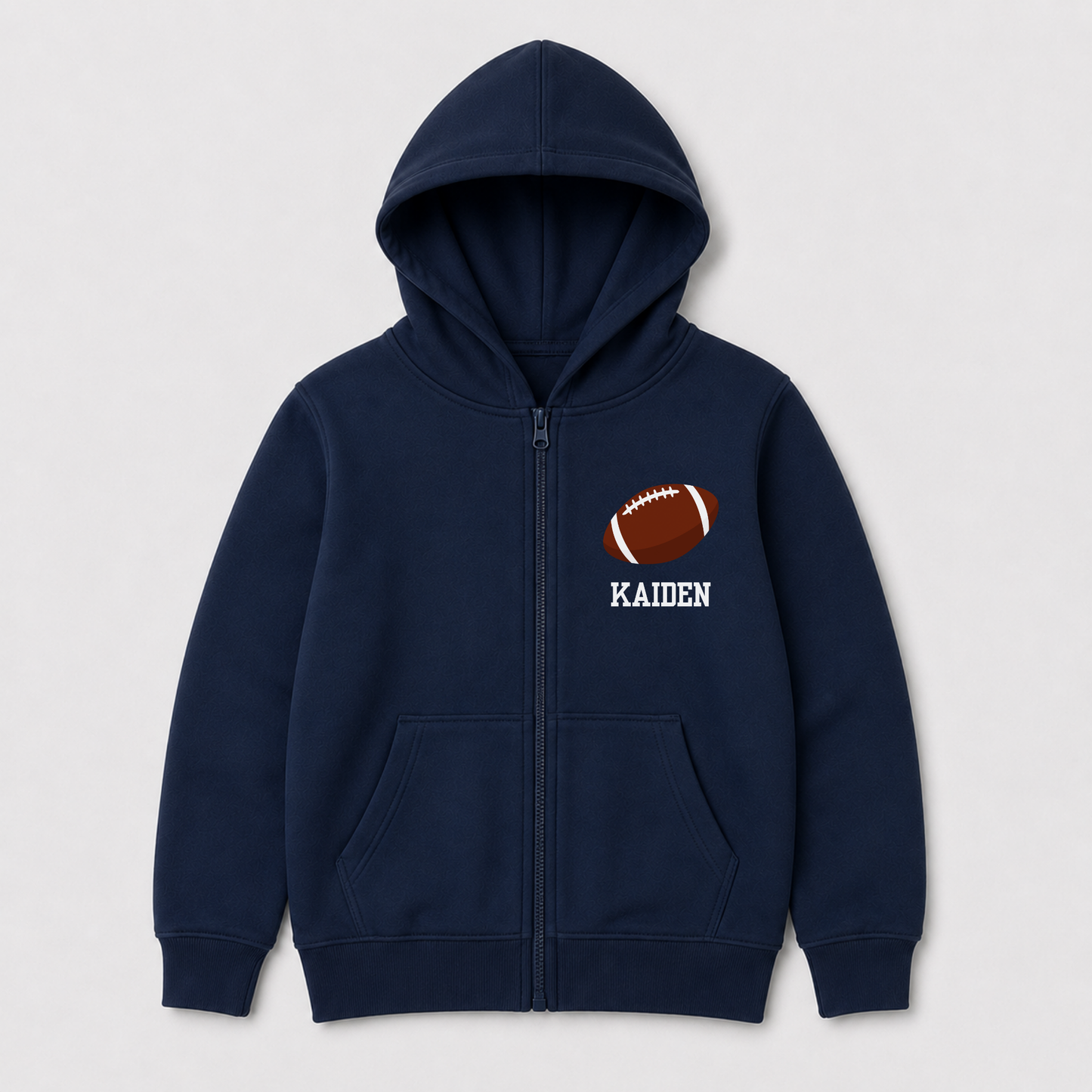 A navy blue zip-up hoodie for kids, featuring a brown and white football graphic on the left chest with the name 'KAIDEN' printed in white underneath, shown against a light gray background.