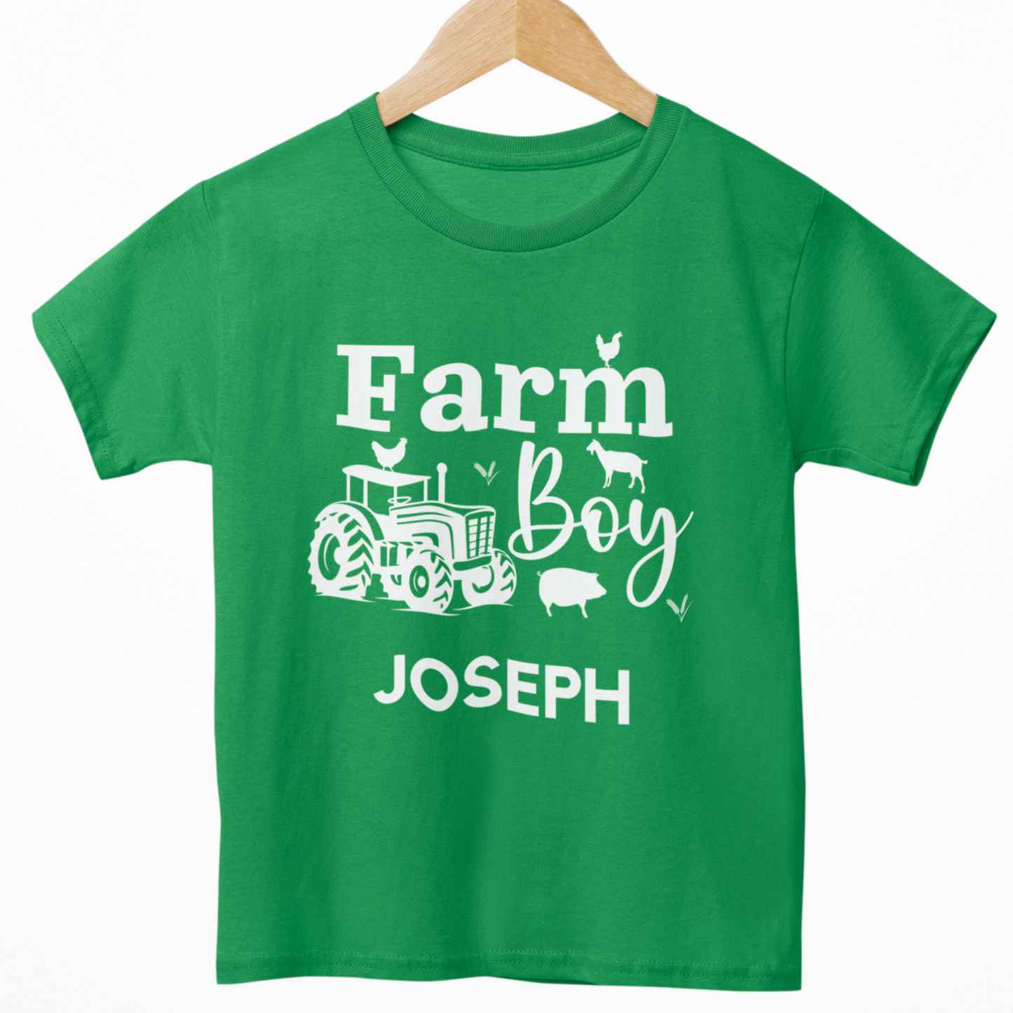 Kids green “Farm Boy” T-shirt with white tractor and farm animals design, personalised with the name in white text underneath. Styled on a wooden hanger.